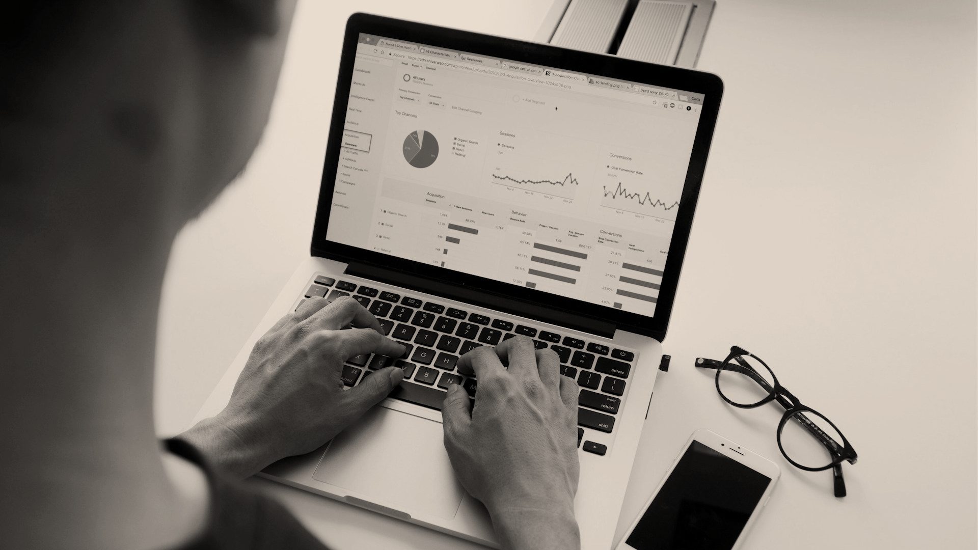 Pessoa digitando num notebook com relatórios de tráfego do site na tela, em tons de cinza